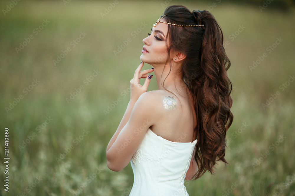 Portrait of beautiful happy young bride is wearing head decor in field over sunset lights