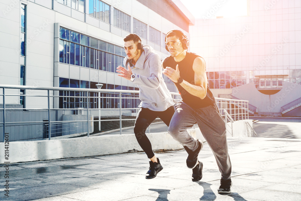 Obraz premium Two friends on a morning run. Young athletes involved in sports in the city. The sun's beam hits the frame. The photo represents a healthy lifestyle and sport.
