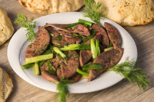 lamb liver food with green vegetables in the plate and local bread on the wooden table for restaurant and kitchen concept.