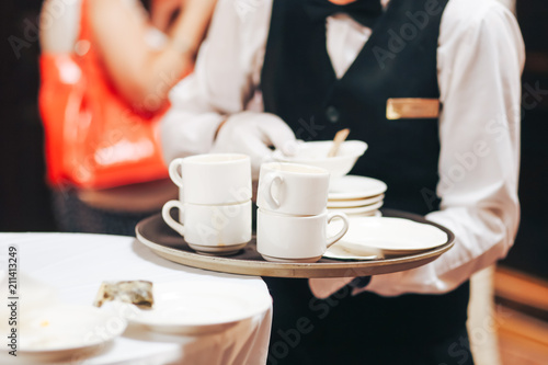 the waiter holds a tray with dirty cups under the coffee