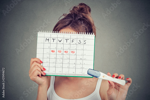 woman hiding behind a periods calendar and showing a positive pregnancy test photo