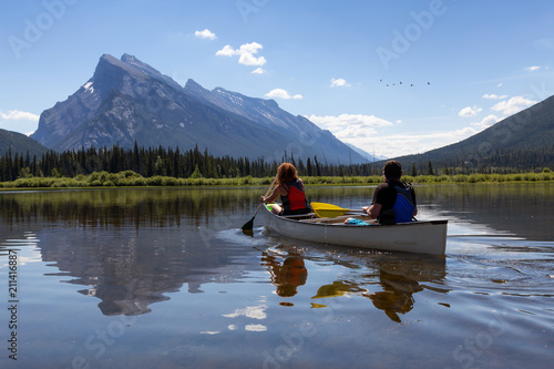 Couple adventurous friends are canoeing in a lake surrounded by the Canadian Mountains. Taken in Vermilion Lakes, Banff, Alberta, Canada. © edb3_16