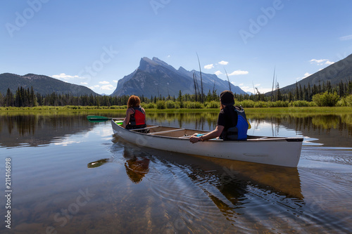 Couple adventurous friends are canoeing in a lake surrounded by the Canadian Mountains. Taken in Vermilion Lakes, Banff, Alberta, Canada.