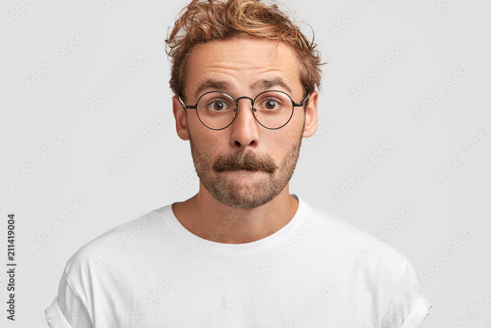 Headshot of puzzled young male presses lips and looks in bewilderment, feels puzzlement, has hesitant expression, contemplates about something, dressed casually, poses against white background Headshot of puzzled young male presses lips and looks in bewilderment, feels puzzlement, has hesitant expression, contemplates about something, dressed casually, poses against white background
