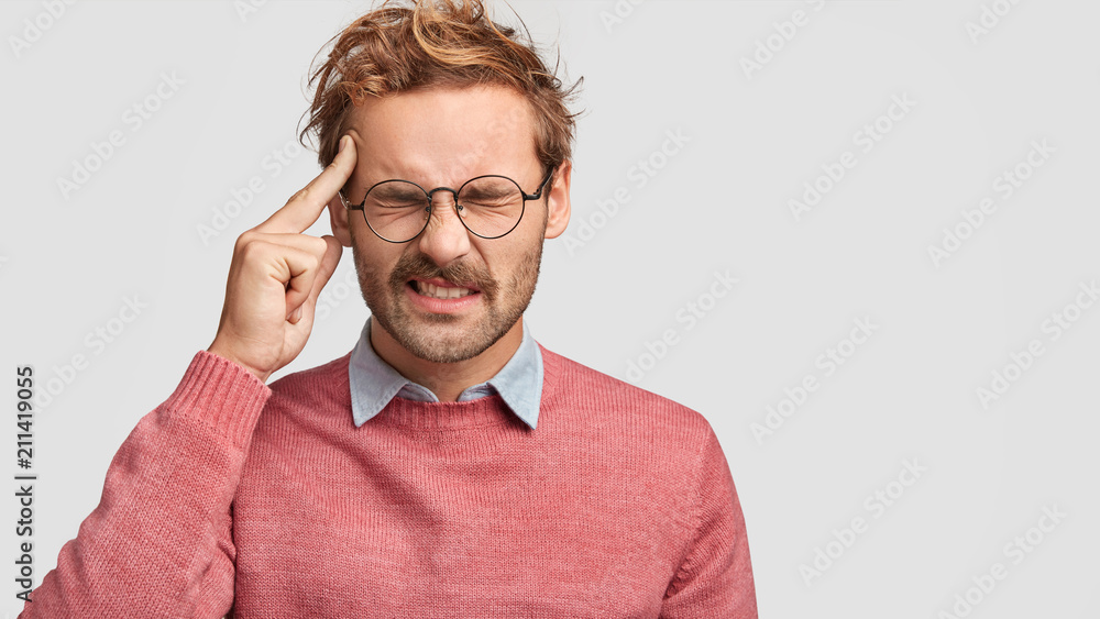 Photo of stressed male feels pressure as being overworked, keeps index finger on temple, has headache, frowns face, isolated over white background with copy space for your advertising content - obrazy, fototapety, plakaty 