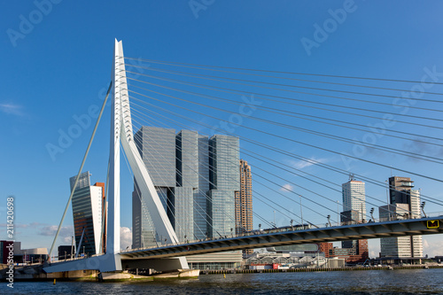 Cityscape of Rotterdam at sunset with the Erasmus bridge in the foreground and high rise buildings of the financial district in the Dutch city in the background against a clear blue sky