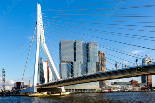 Cityscape of Rotterdam at sunset with the Erasmus bridge in the foreground and high rise buildings of the financial district in the Dutch city in the background against a clear blue sky