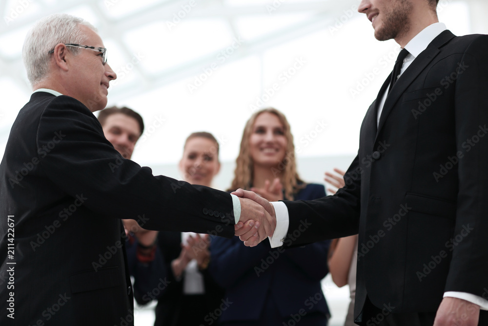 closeup of handshake of business partners on background of employees closeup of handshake of business partners on background of employees