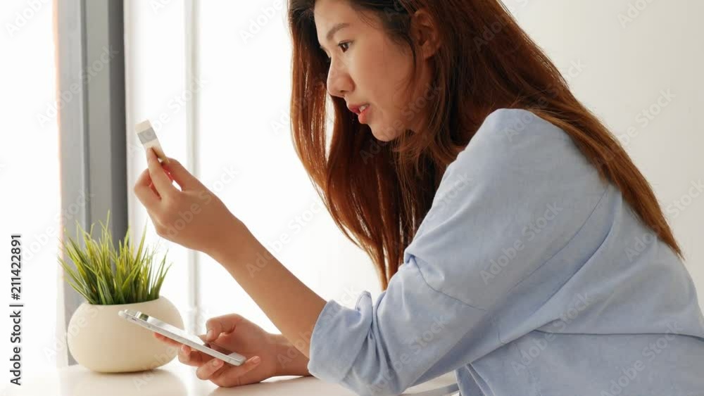 Young asian young woman smiling with smartphone and credit card beside the window at home. Beautiful woman shopping online with credit card. Young asian young woman smiling with smartphone and credit card beside the window at home. Beautiful woman shopping online with credit card.