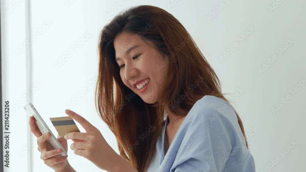 Young asian young woman smiling with smartphone and credit card beside the window at home. Beautiful woman shopping online with credit card. Young asian young woman smiling with smartphone and credit card beside the window at home. Beautiful woman shopping online with credit card.