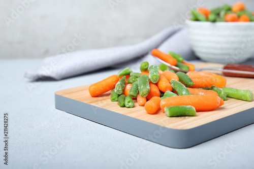 Wooden board with frozen vegetables on table