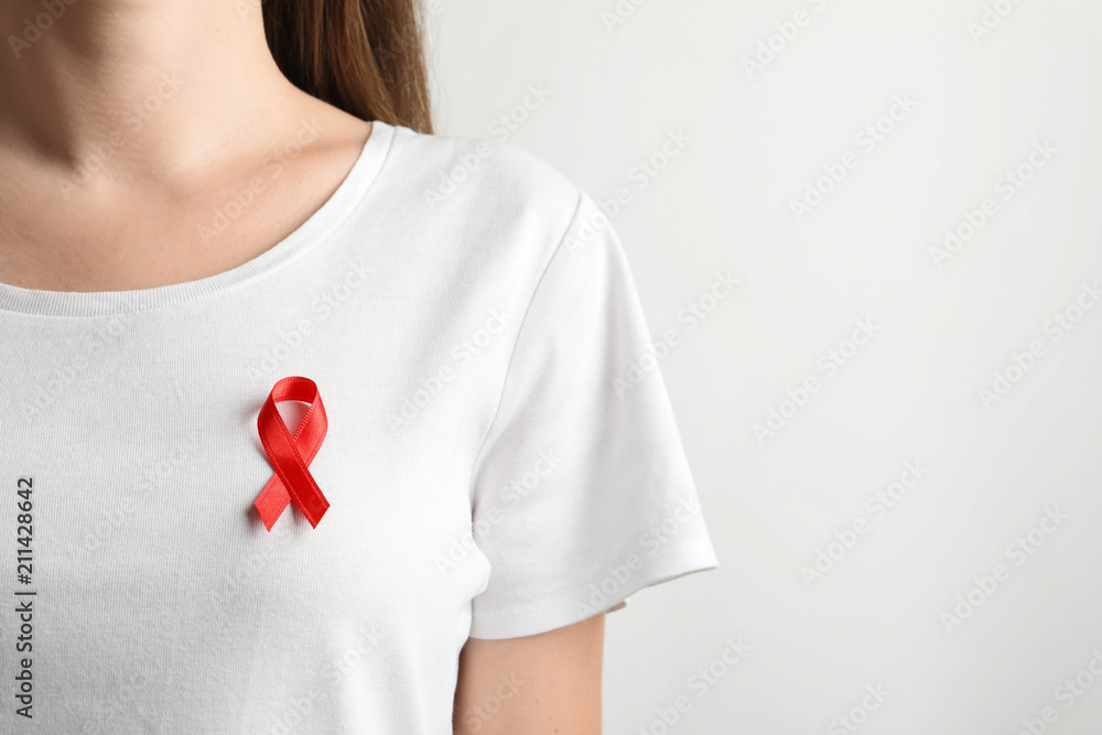 Woman with red ribbon on t-shirt against light background. Cancer awareness Woman with red ribbon on t-shirt against light background. Cancer awareness