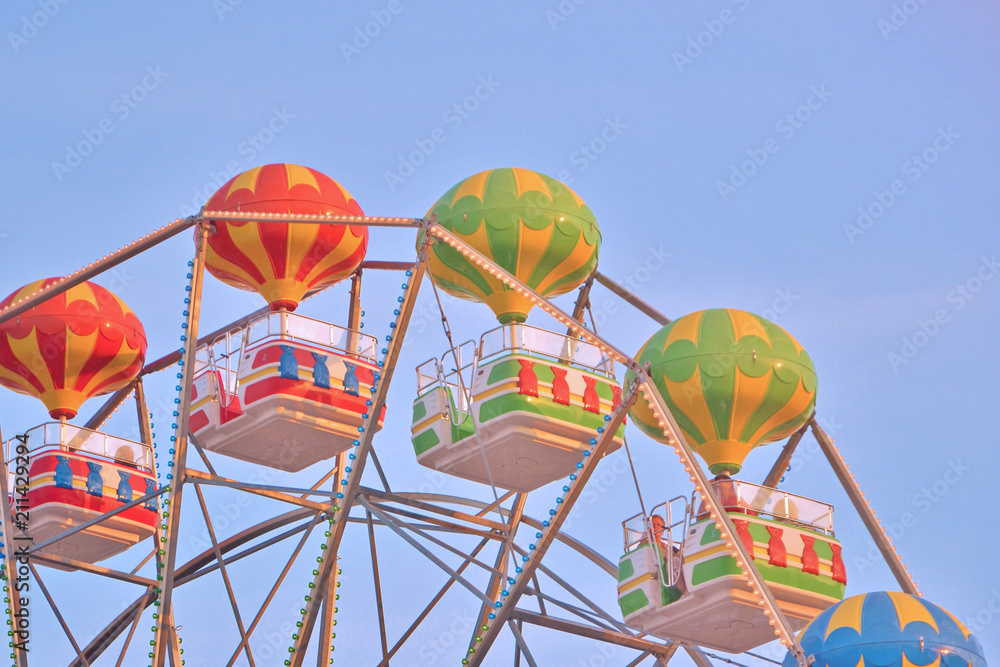Fototapeta premium Multicolored booths of a ferris wheel over a blue sky background with a sunny day. Seafront in Bulgaria, Golden Sands.