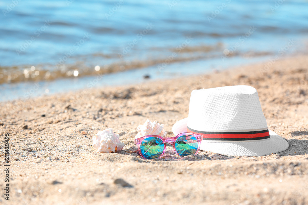 Hat, sunglasses and shells on sand near sea. Beach object Hat, sunglasses and shells on sand near sea. Beach object