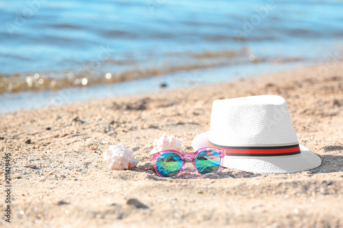 Hat, sunglasses and shells on sand near sea. Beach object