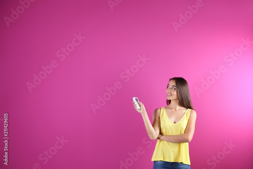 Young woman switching on air conditioner on color background