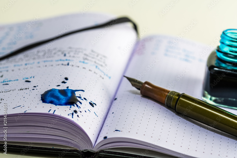 Notebook with writing and a fountain pen with blue ink, ink splattered on the paper making a mess and a large blue ink blot Notebook with writing and a fountain pen with blue ink, ink splattered on the paper making a mess and a large blue ink blot