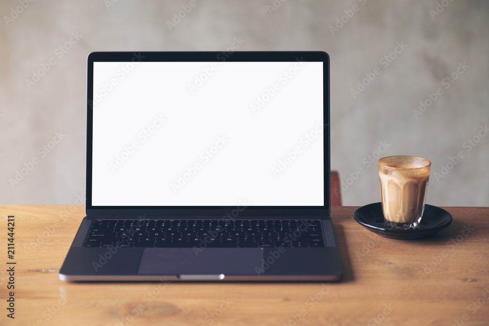 Mockup image of laptop with blank white desktop screen and coffee cup on wooden table with concrete wall background Mockup image of laptop with blank white desktop screen and coffee cup on wooden table with concrete wall background