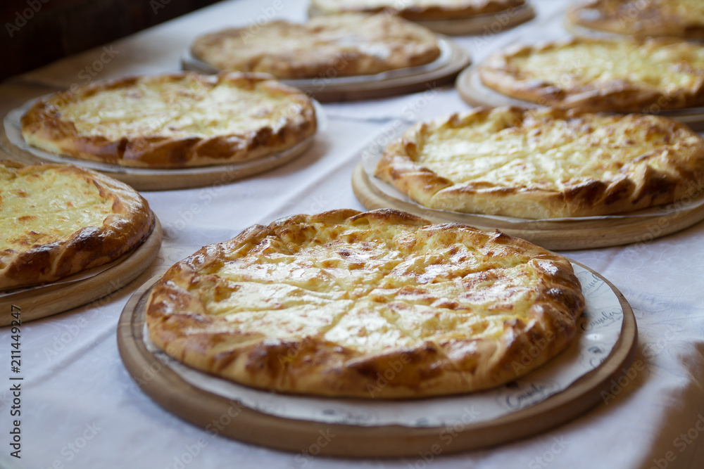hot appetizing delicious pies topped with cheese and laying on a long table covered with white tablecloth hot appetizing delicious pies topped with cheese and laying on a long table covered with white tablecloth