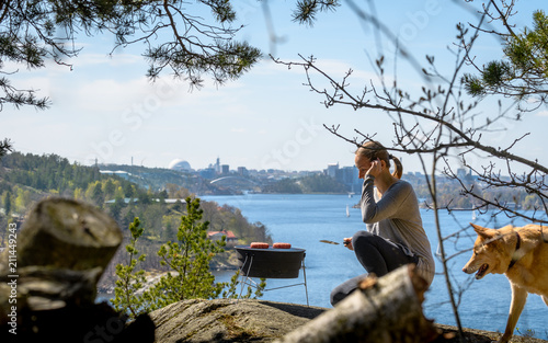 Woman grilling hamburger on charcoal barbecue in front of Stockholm skyline