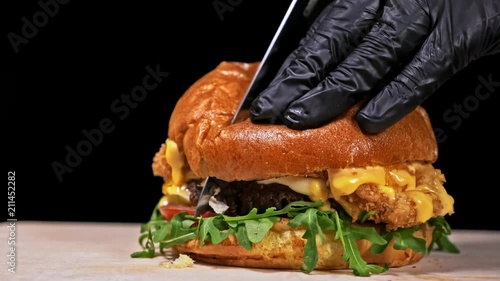 Burger is cooking on black background in black food gloves. Very luscious air bun and marbled beef. Restaurant where each burgers is cooked by hand. Burger cut on the table with a knife. Not made photo