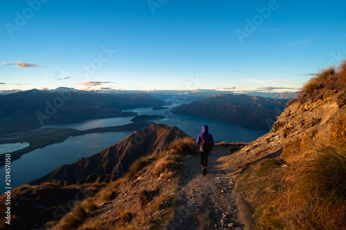 A hiker hiking on the beautiful track with a landscape of the mountains and Lake Wanaka. Roys Peak Track, South Island, New Zealand. © Klanarong Chitmung