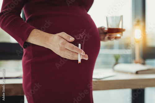 Damaging habit. Young irresponsible woman drinking alcohol and smoking while being pregnant