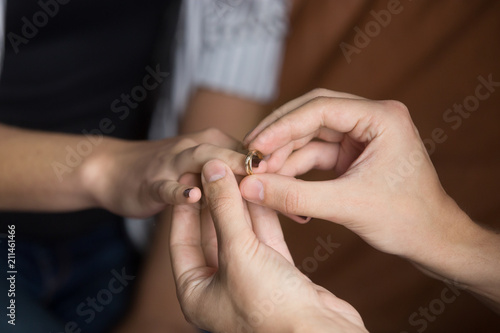 Close up of man putting wedding ring on woman finger making marriage proposal to beloved, boyfriend proposing to girlfriend, lovers couple getting married or engaged. Concept of engagement