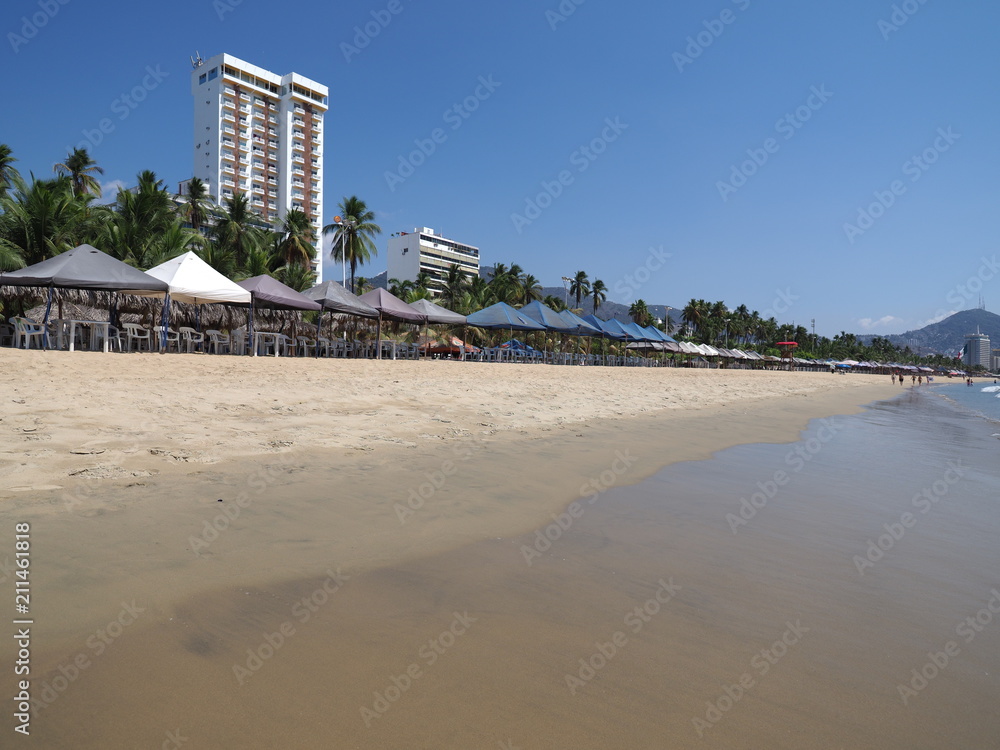 High white hotel and umbrellas on sandy beach at bay of Acapulco city landscape in Mexico at Pacific Ocean