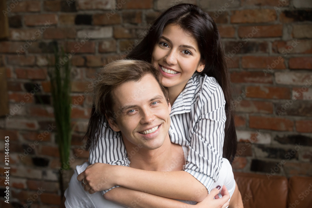 Portrait of smiling couple looking at camera, hugging posing for family album, spouses embracing showing support, boyfriend giving piggyback ride to happy girl spending time together at home Portrait of smiling couple looking at camera, hugging posing for family album, spouses embracing showing support, boyfriend giving piggyback ride to happy girl spending time together at home