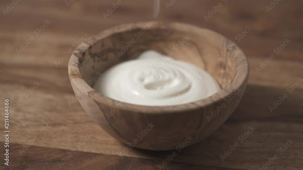 sour cream pour into wood bowl closeup sour cream pour into wood bowl closeup