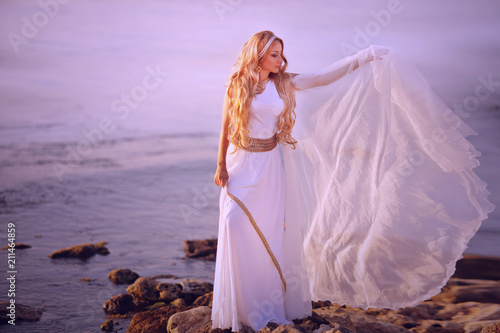 Fototapeta Beautiful girl in a long white wedding dress in Greek style is the old Greek god