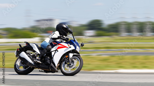The girl in a white jacket and blue jeans race on a motorcycle. Motion blur. Copyspace.
