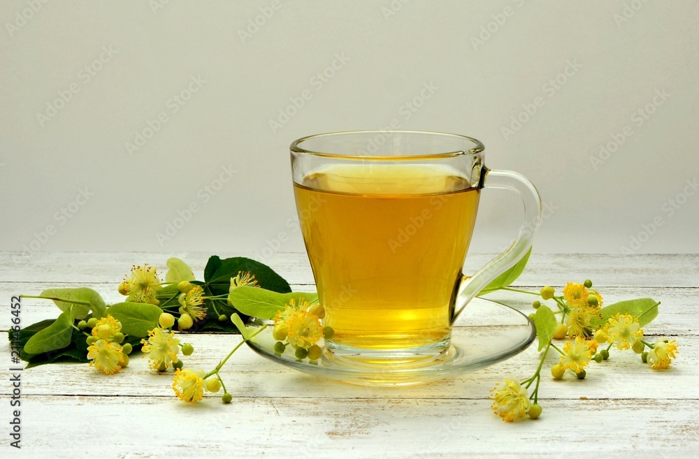 Tea with linden flowers in a transparent cup on a white wooden table with linden branches. Tea with linden flowers in a transparent cup on a white wooden table with linden branches.