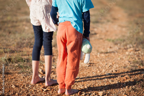 little boy with toy in hand and girl barefooted refugees standing in hot desert