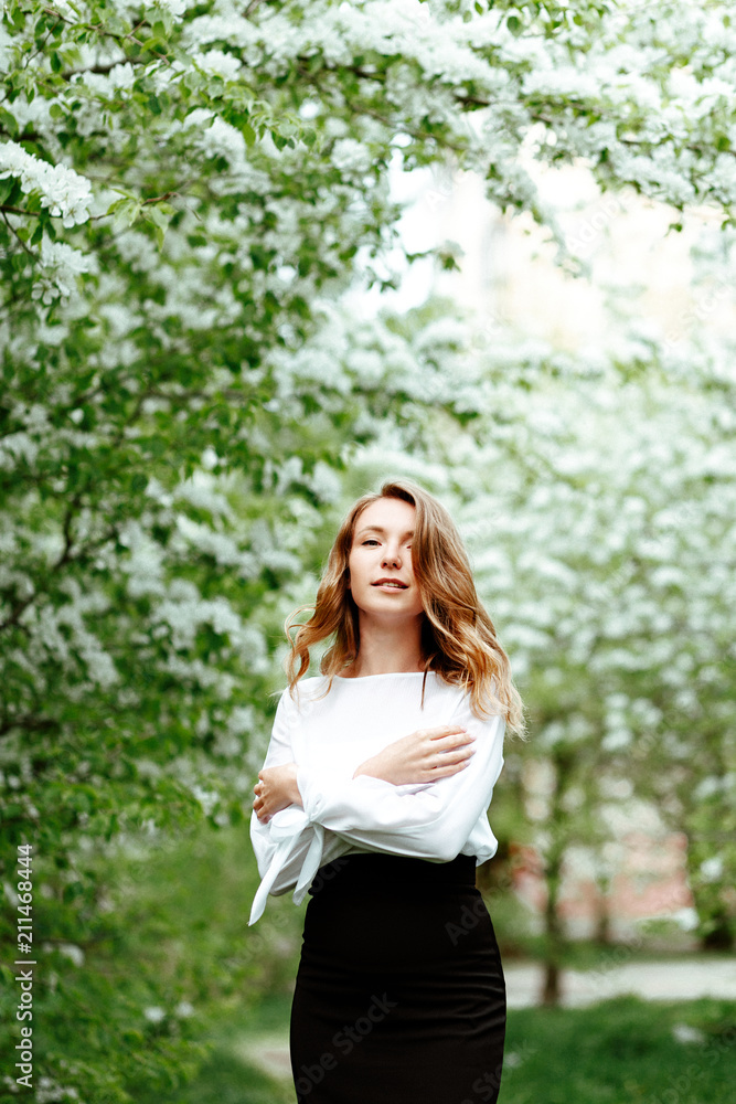 Cute spring portrait. Young business woman in a business office suit on the background of Apple trees in bloom. Cute spring portrait. Young business woman in a business office suit on the background of Apple trees in bloom.