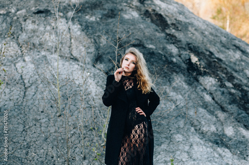 фотографія Portrait of a sexy young woman in a black dress with a bright evening make-up on the background of a lifeless desert