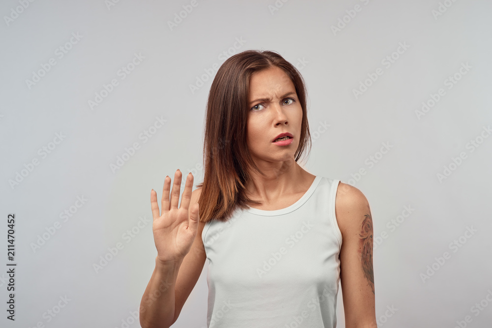 Body language. Stressed out woman wearing her blonde hair loose posing against gray studio wall, keeping hands in stop gesture, trying to defend herself as if saying: Stop that, Stay away from me Body language. Stressed out woman wearing her blonde hair loose posing against gray studio wall, keeping hands in stop gesture, trying to defend herself as if saying: Stop that, Stay away from me