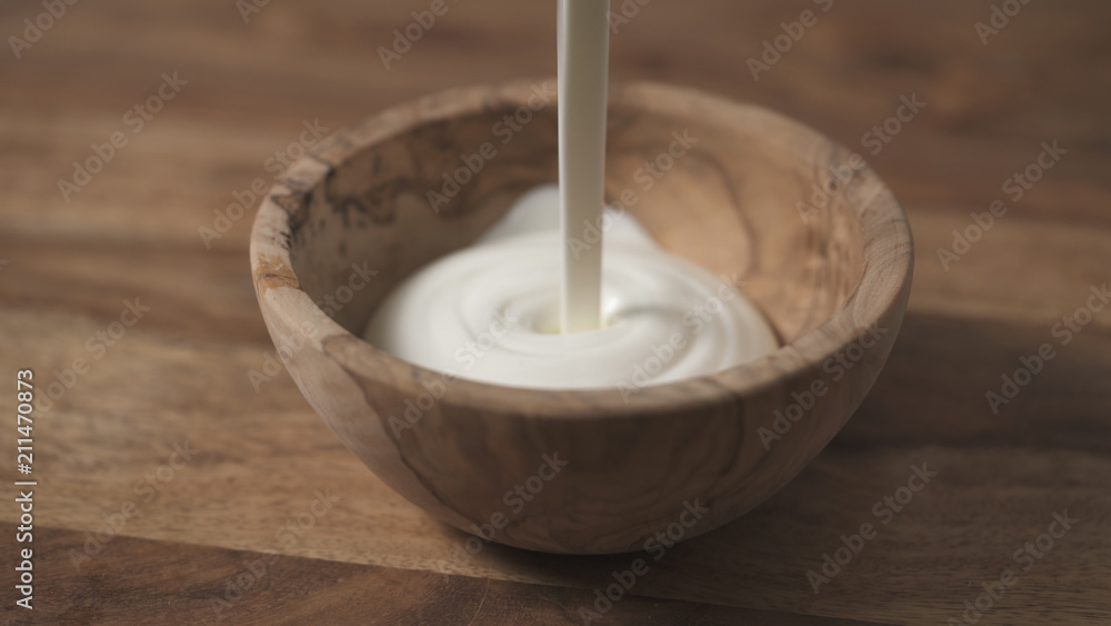 sour cream pour into wood bowl closeup sour cream pour into wood bowl closeup