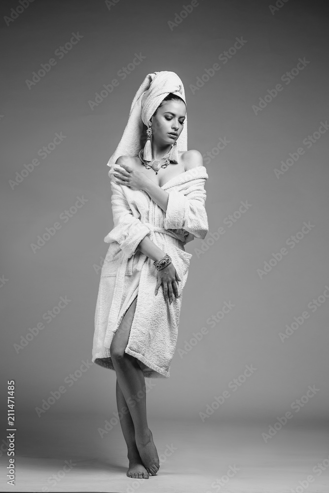 Young woman in a bathrobe and towel on her head, fashion golden jewelry, spa and care portrait, clean natural face, portrait on a background isolated Young woman in a bathrobe and towel on her head, fashion golden jewelry, spa and care portrait, clean natural face, portrait on a background isolated