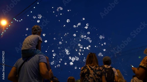 The child sits on the daddy's neck and looks at the firework