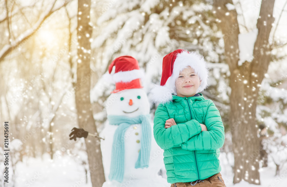 portrait of smiling boy in red christmas hat with snowman on background. Space for text