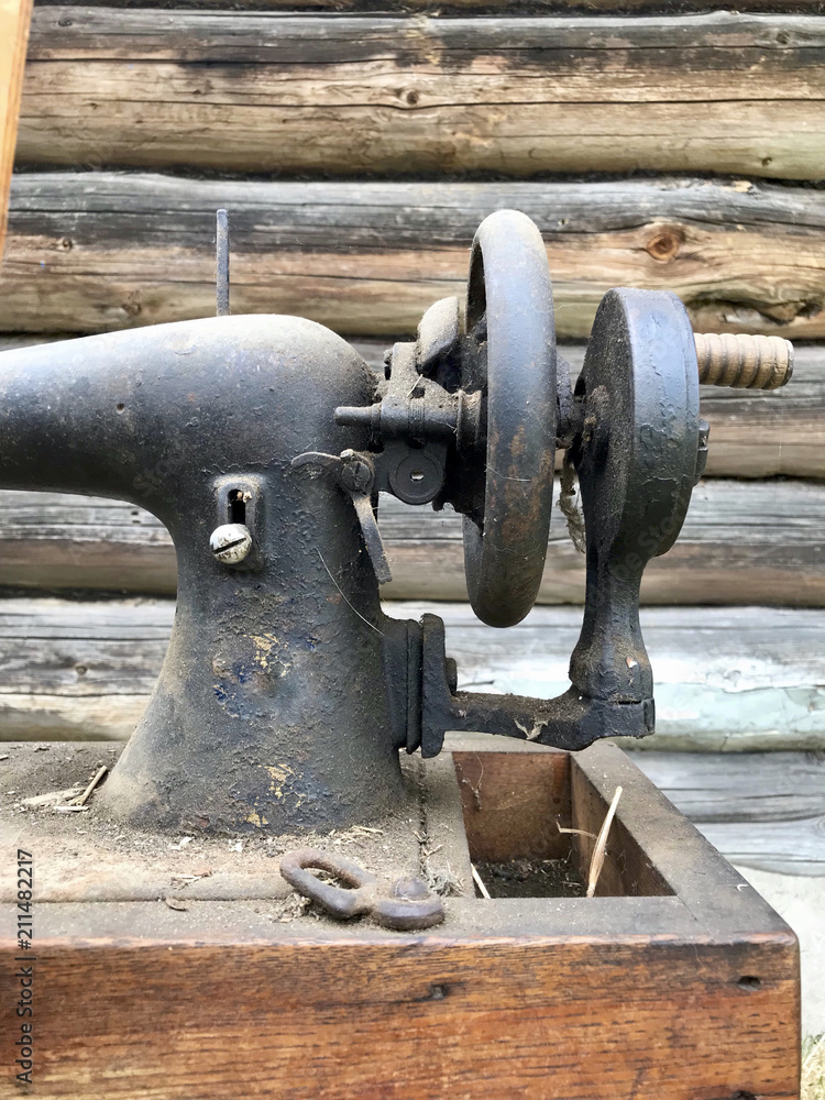 Hand drive old sewing machine close-up. Covered with corrosion, dust and cobwebs. Against the background of a wooden abandoned barn. Hand drive old sewing machine close-up. Covered with corrosion, dust and cobwebs. Against the background of a wooden abandoned barn.