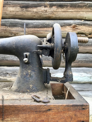 Hand drive old sewing machine close-up. Covered with corrosion, dust and cobwebs. Against the background of a wooden abandoned barn.