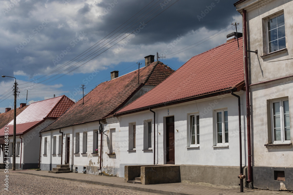 Street in Tykocin with white historic houses in front of the synagogue under the dramatic cloudy sky