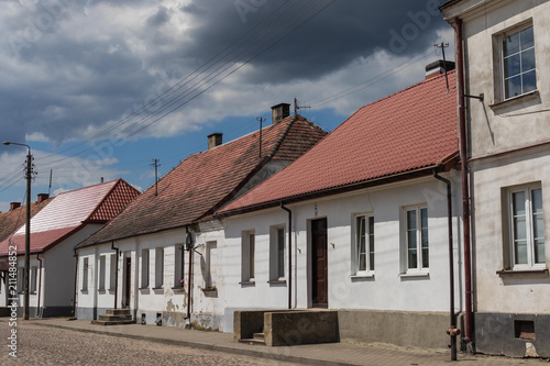 Street in Tykocin with white historic houses in front of the synagogue under the dramatic cloudy sky