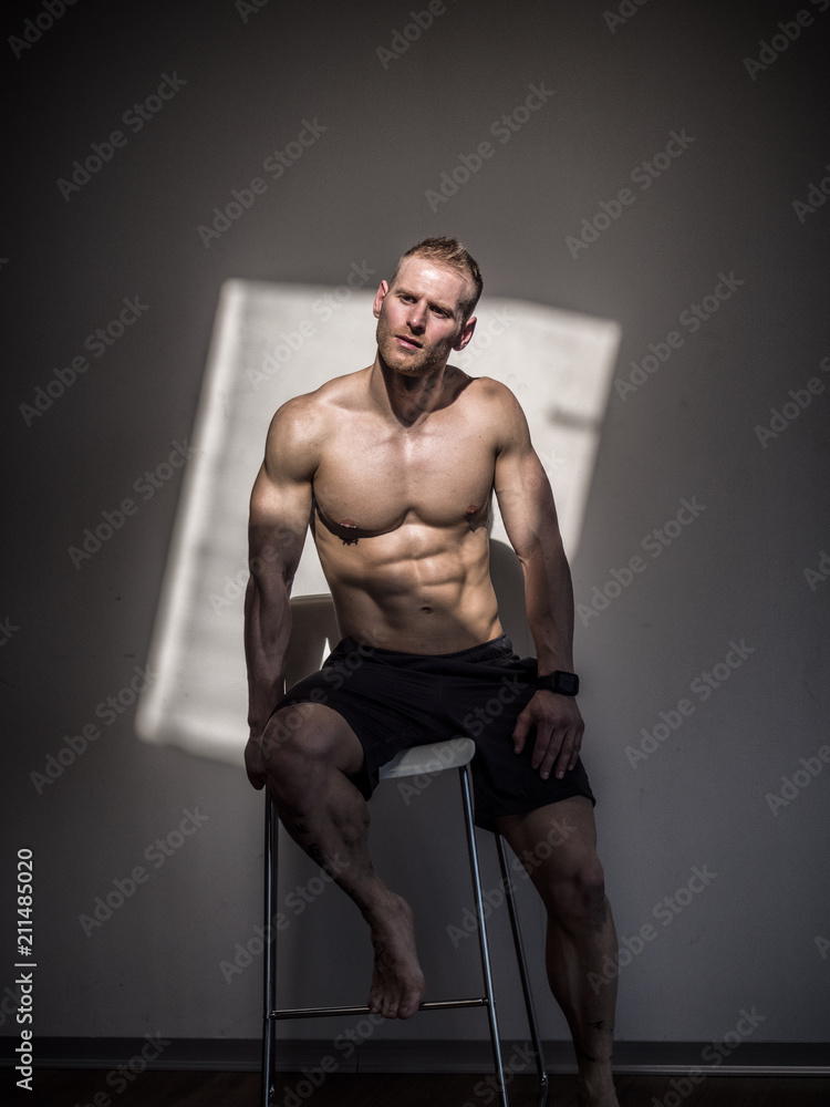 Attractive shirtless blond male bodybuilder in shorts indoors in