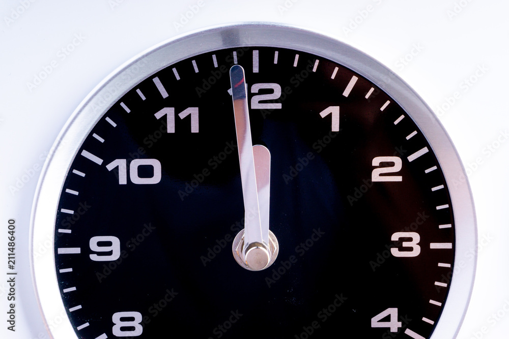 Closeup of modern black chrome clock on white background indicates twelve o'clock, wake up, time for action, time up or midday. Time passing concept for business urgency and running out of time. Closeup of modern black chrome clock on white background indicates twelve o'clock, wake up, time for action, time up or midday. Time passing concept for business urgency and running out of time.