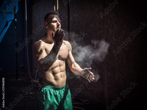 Shirtless man using chalk or magnesium powder in gym, clapping hands and creating cloud