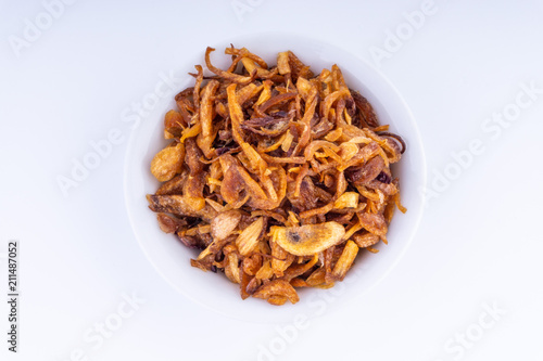 Deep fried shallots crisp / fried crispy onion flakes (bawang goreng) in white bowl over wooden background.